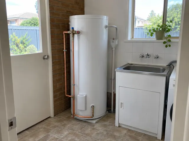 White hot water tank beside a laundry sink with copper pipework and tiled walls in The Ponds