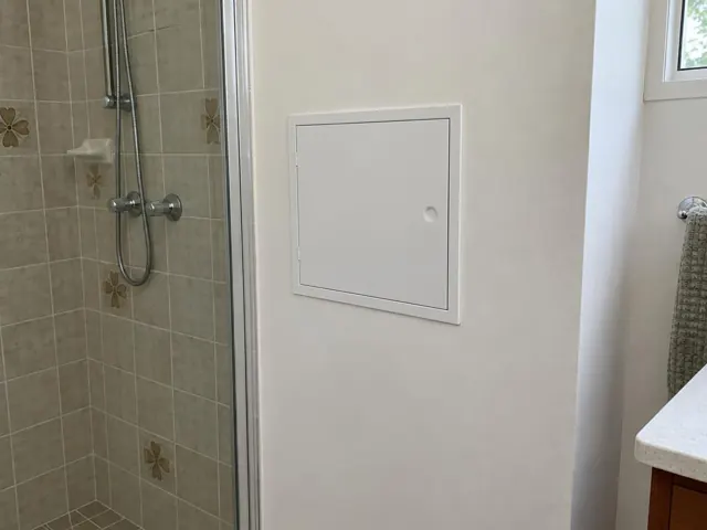 Bathroom wall with a neat access panel beside a tiled shower and vanity in The Ponds